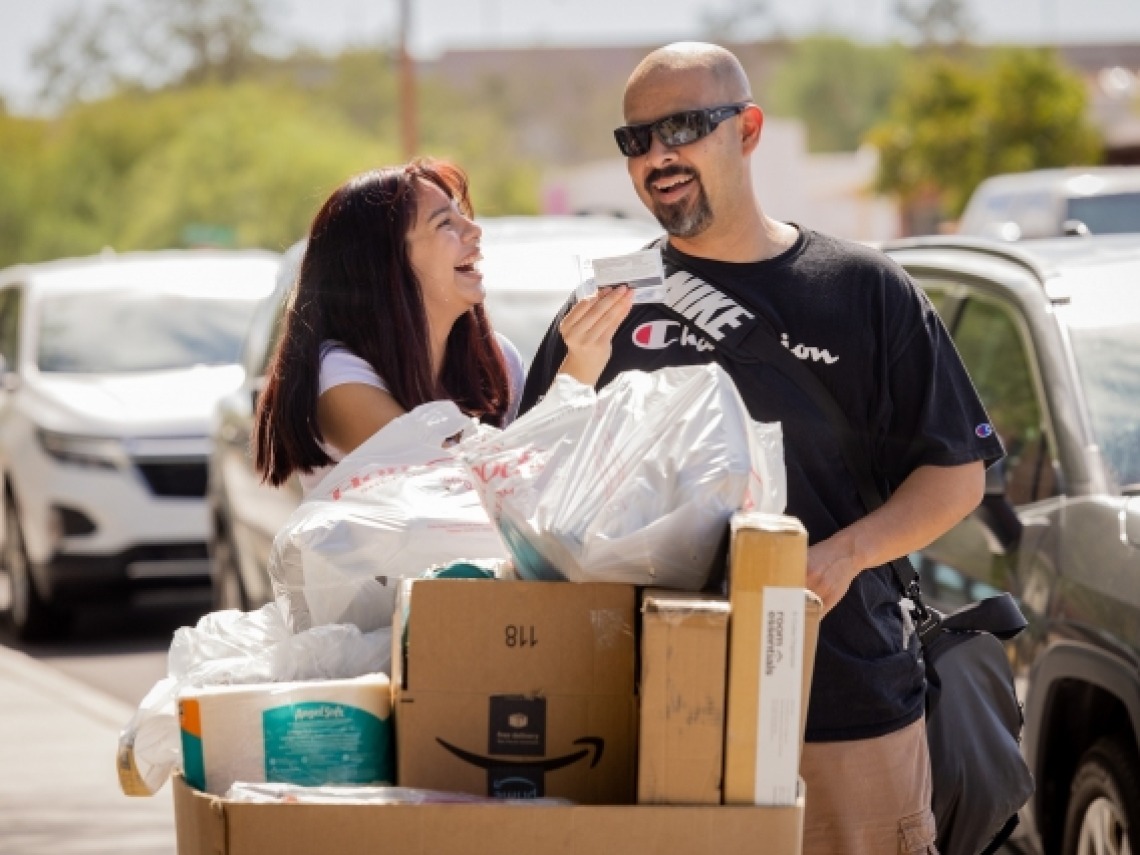 University of Arizona student and her father laughing as they push a bin full of belongings towards a dorm room