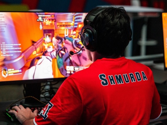 A man wearing headphones and a red shirt that says &quot;Shmurda&quot; on the back plays computer games.