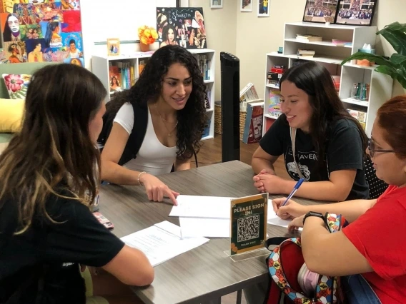 A group of students sit at a desk while talking.