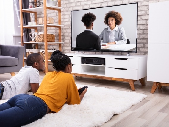 a young Black couple watches two Black characters on a TV screen
