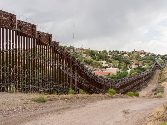 A metal fence covered in barbed wire runs horizontally across the photo with a trail running alongside it.