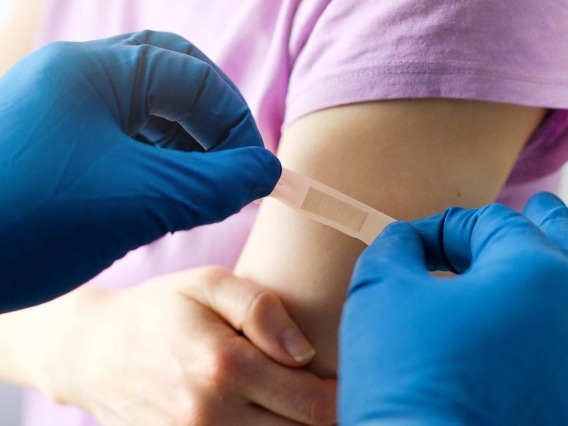 A person wearing blue medical gloves applies a bandage to someone&#039;s arm.