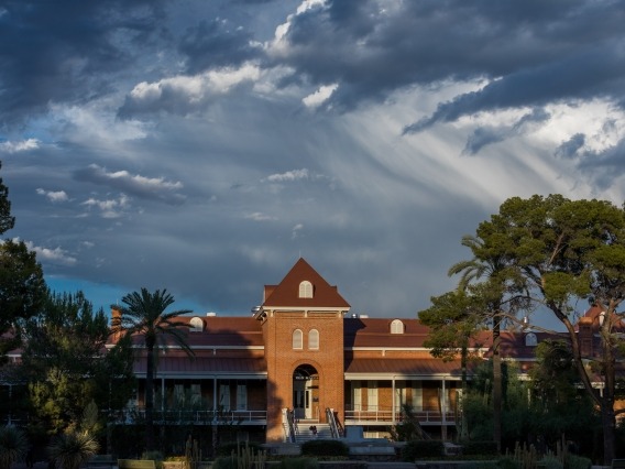 clouds part above old main, allowing sunlight to shine down on the building and surrounding trees